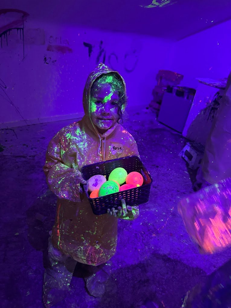 A young girl in a paint-covered poncho holding neon paint props during top things to do in Liverpool as a Creative Activities for Kids